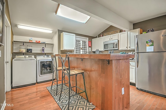 kitchen with washing machine and clothes dryer, a kitchen bar, lofted ceiling with beams, stainless steel appliances, and white cabinetry