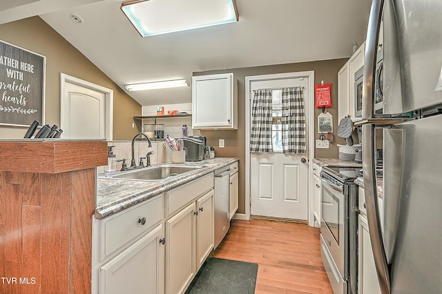 kitchen with light countertops, vaulted ceiling, appliances with stainless steel finishes, light wood-style floors, and a sink