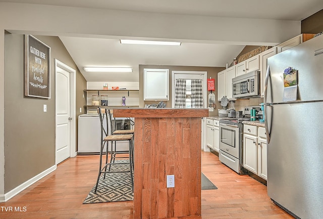 kitchen with stainless steel appliances, lofted ceiling, white cabinets, and light wood-style flooring