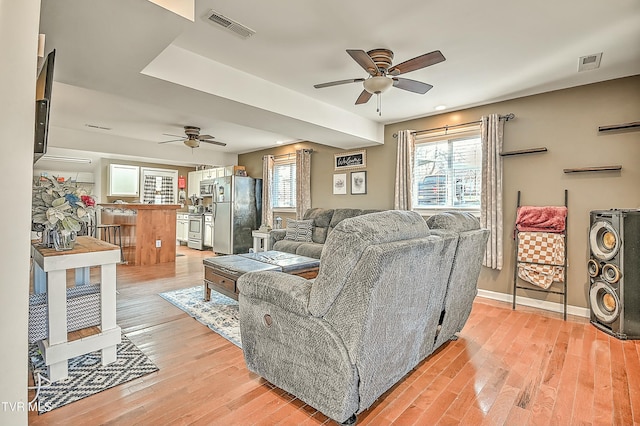 living room featuring light wood-type flooring, visible vents, and a ceiling fan