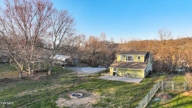 view of front of property with a view of trees, a fire pit, a fenced backyard, and a front lawn