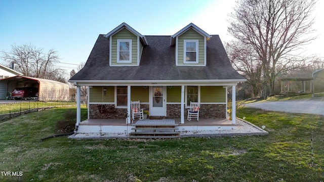 cape cod home with stone siding, covered porch, a front yard, and a shingled roof