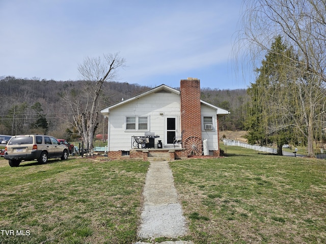 view of front of property featuring a wooded view, a chimney, a front lawn, and fence