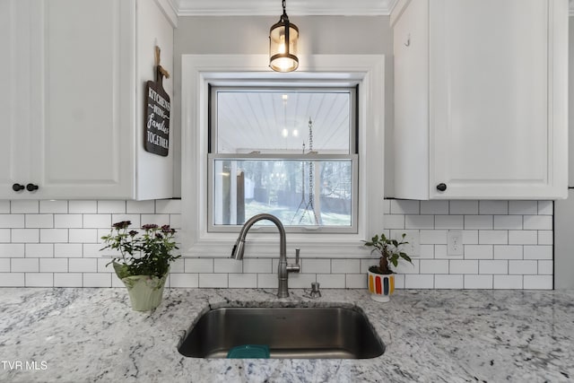 kitchen with light stone countertops, a sink, white cabinets, crown molding, and backsplash