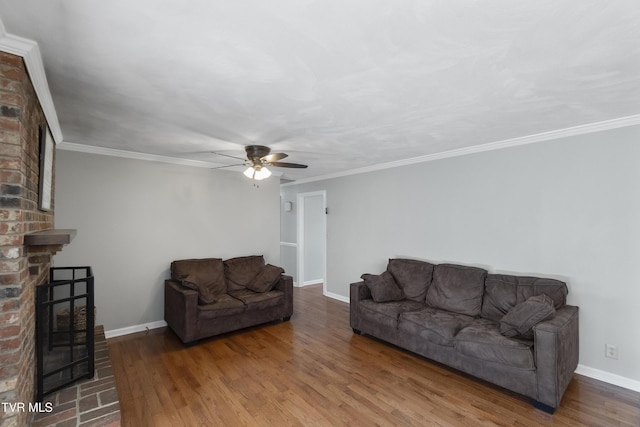 living room featuring wood finished floors, baseboards, ceiling fan, crown molding, and a brick fireplace