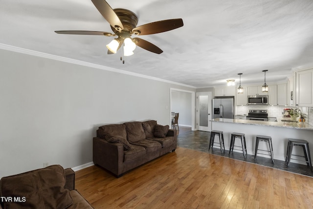 living area with baseboards, wood finished floors, a ceiling fan, and ornamental molding