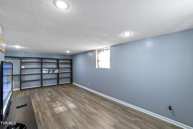 basement with visible vents, a textured ceiling, baseboards, and wood finished floors