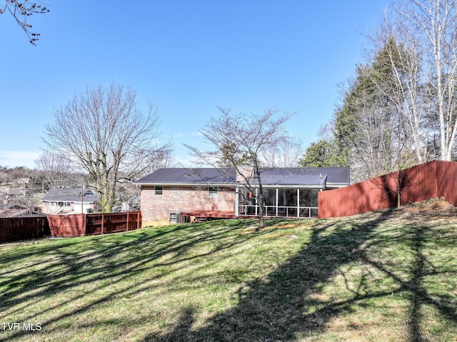 back of property featuring metal roof, fence, a lawn, and a sunroom