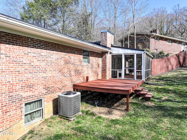 back of house featuring brick siding, central AC, a chimney, a yard, and a sunroom