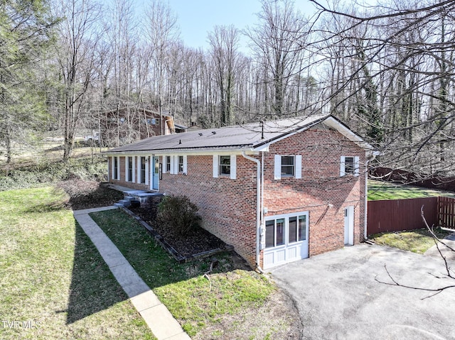 view of side of home featuring brick siding, fence, a lawn, driveway, and an attached garage