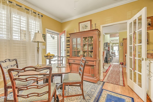 dining space with french doors, light wood-style floors, and crown molding