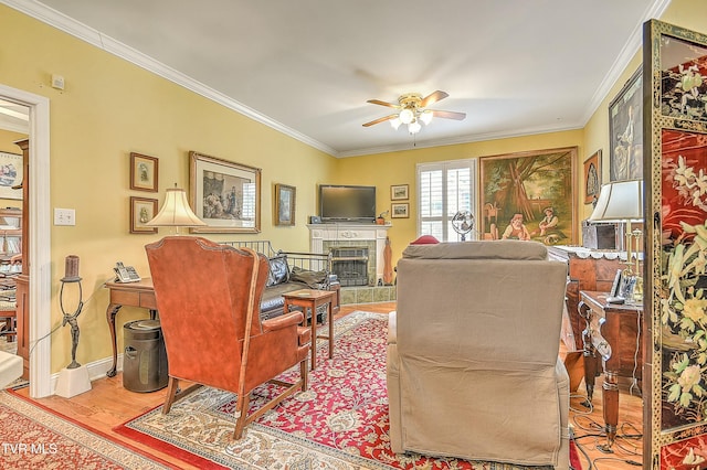 living room featuring a tile fireplace, crown molding, a ceiling fan, and wood finished floors