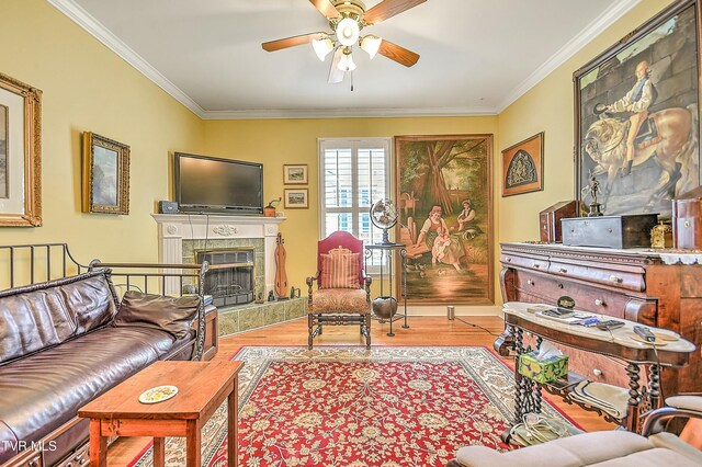 living room featuring a tiled fireplace, crown molding, wood finished floors, and a ceiling fan