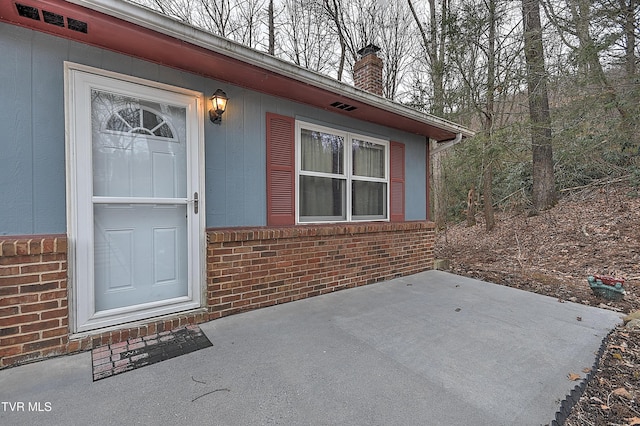 entrance to property featuring visible vents, brick siding, and a chimney