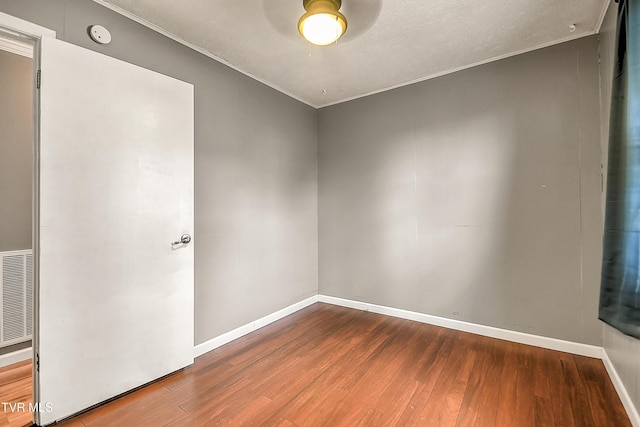 empty room featuring crown molding, wood finished floors, visible vents, and baseboards