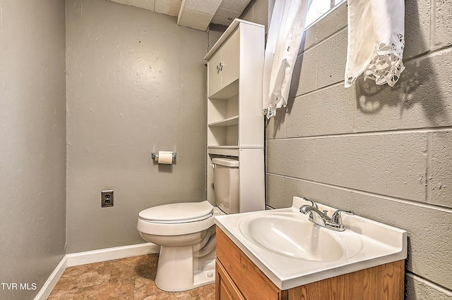 bathroom featuring stone finish flooring, toilet, vanity, and baseboards