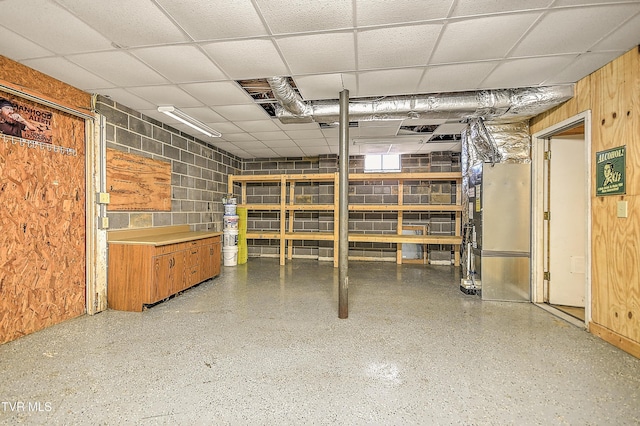 basement featuring a drop ceiling, wooden walls, and concrete block wall