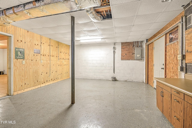 unfinished basement with electric panel, wooden walls, concrete block wall, and a drop ceiling