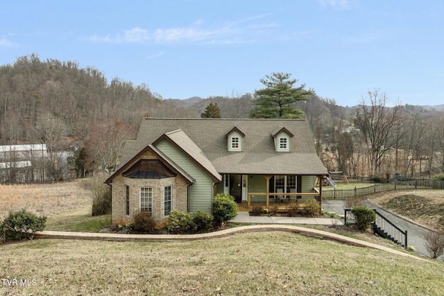 view of front of home featuring a front yard, fence, covered porch, and a shingled roof