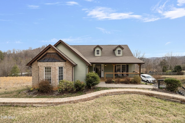 view of front of home with a front yard, roof with shingles, a porch, and brick siding