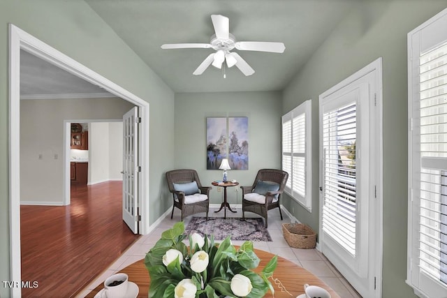 living area featuring light tile patterned floors, a ceiling fan, and baseboards