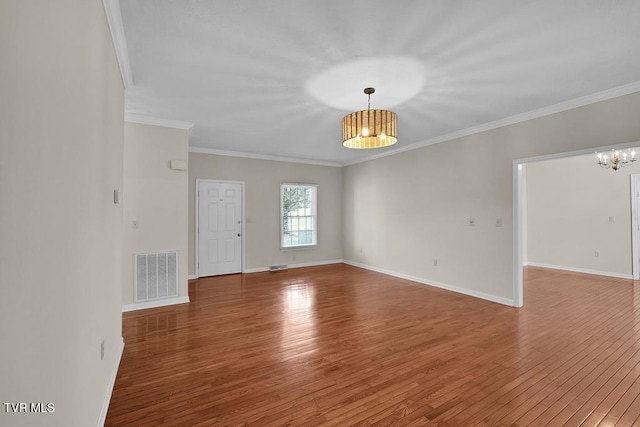 spare room featuring wood finished floors, visible vents, baseboards, crown molding, and a notable chandelier