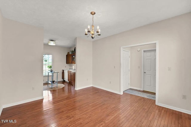 empty room featuring hardwood / wood-style floors, a notable chandelier, and baseboards