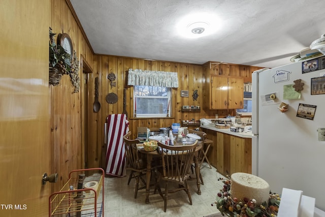 kitchen with light floors, freestanding refrigerator, wood walls, a textured ceiling, and brown cabinets