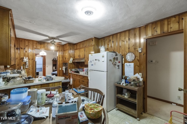 kitchen with wood walls, ceiling fan, brown cabinetry, and freestanding refrigerator