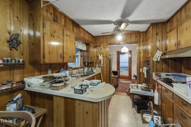 kitchen with a ceiling fan, a sink, brown cabinetry, light countertops, and stainless steel oven