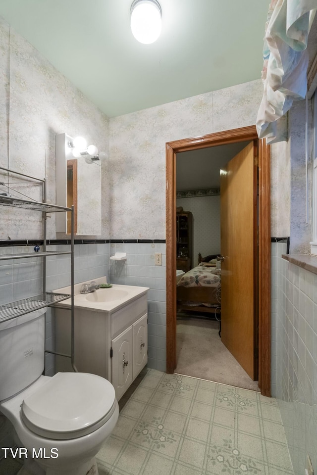 bathroom featuring vanity, wallpapered walls, ensuite bathroom, tile walls, and toilet