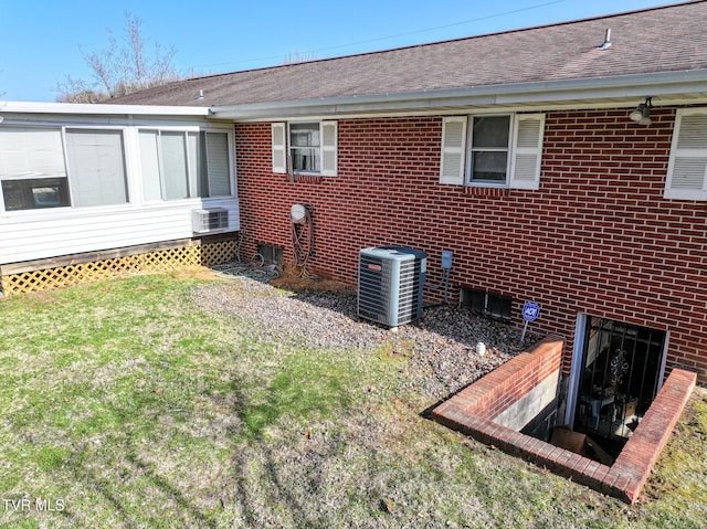 rear view of property featuring brick siding, roof with shingles, central AC unit, and a lawn