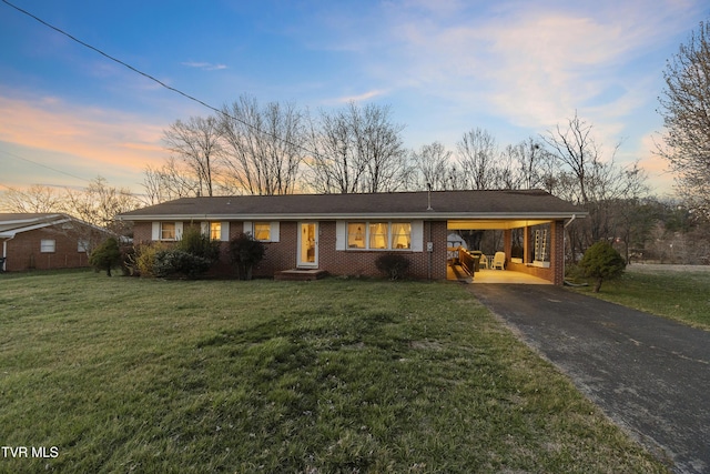 view of front facade with brick siding, an attached carport, driveway, and a front lawn