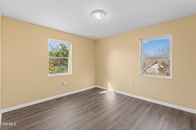 spare room featuring dark wood finished floors, visible vents, and baseboards