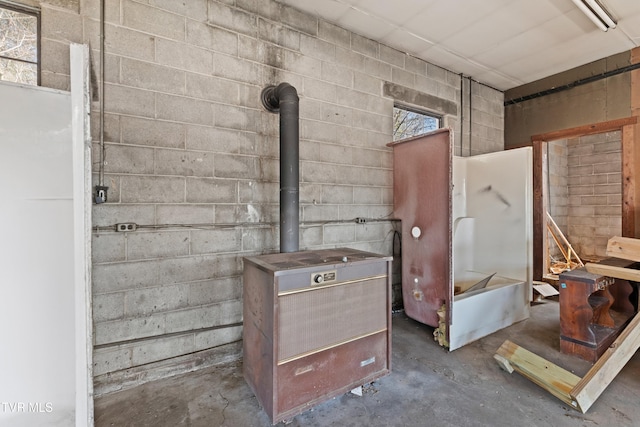 bathroom featuring a wood stove, concrete block wall, and unfinished concrete floors