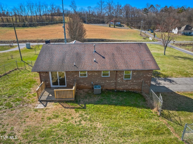 back of property featuring cooling unit, fence, roof with shingles, a yard, and brick siding