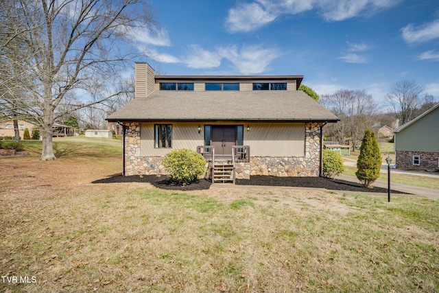 view of front of house with a shingled roof, a front lawn, stone siding, and a chimney