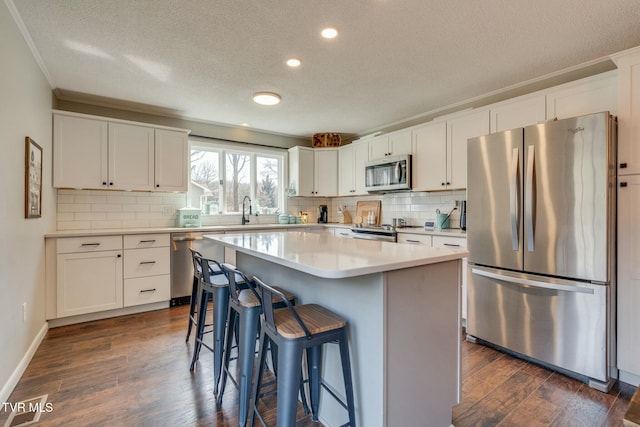 kitchen featuring a sink, a kitchen breakfast bar, dark wood finished floors, white cabinetry, and appliances with stainless steel finishes