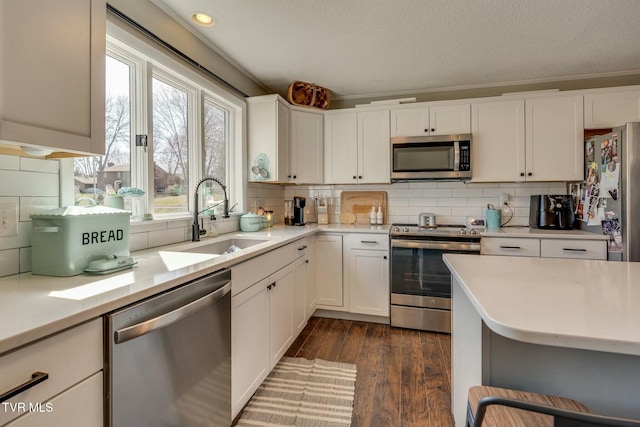 kitchen featuring a sink, backsplash, stainless steel appliances, light countertops, and dark wood-style flooring