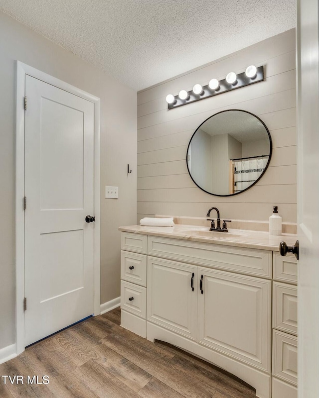 bathroom with vanity, wooden walls, wood finished floors, and a textured ceiling