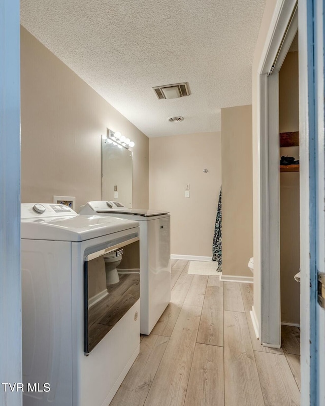 laundry room featuring visible vents, laundry area, a textured ceiling, light wood-type flooring, and washer and clothes dryer