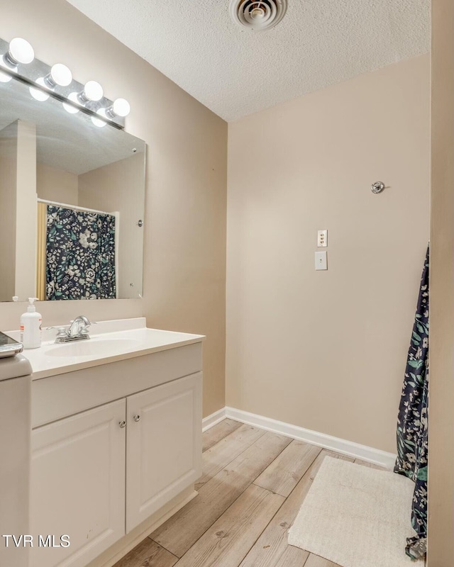 full bath featuring visible vents, a textured ceiling, wood finished floors, baseboards, and vanity