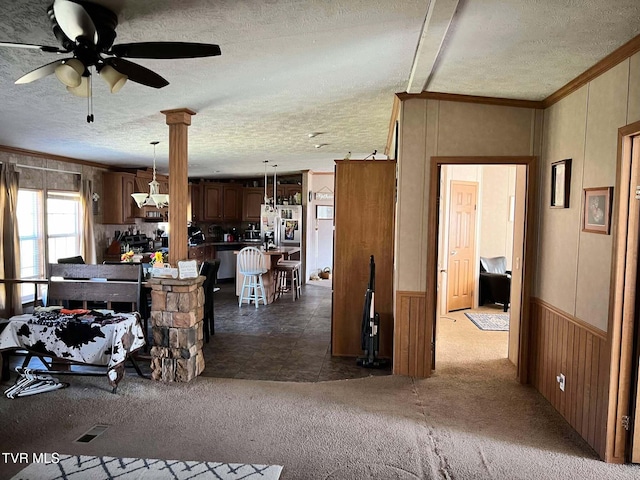 interior space with ceiling fan, a wainscoted wall, ornamental molding, a textured ceiling, and dark colored carpet