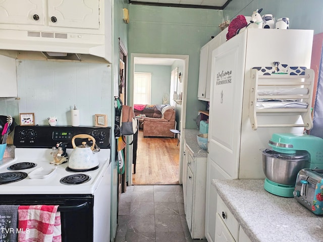 kitchen with freestanding refrigerator, light countertops, white cabinets, under cabinet range hood, and range with electric stovetop