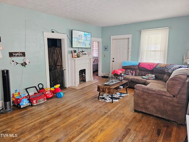 living room featuring a fireplace with flush hearth, wood finished floors, and a textured ceiling