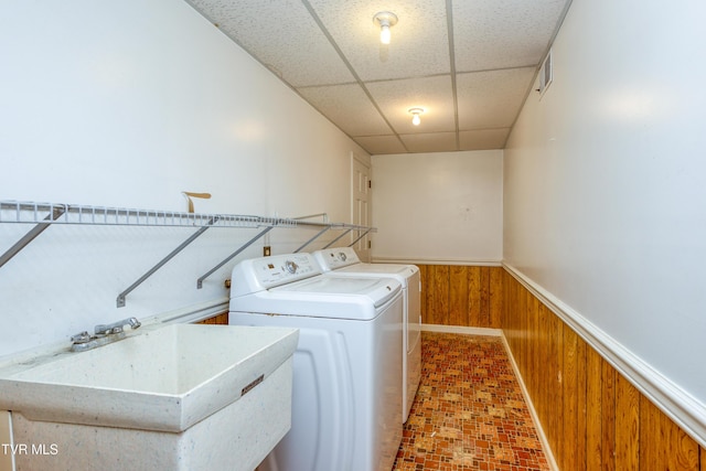 clothes washing area featuring wooden walls, washer and clothes dryer, laundry area, wainscoting, and a sink