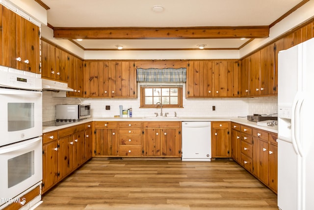 kitchen featuring under cabinet range hood, beam ceiling, brown cabinets, white appliances, and a sink