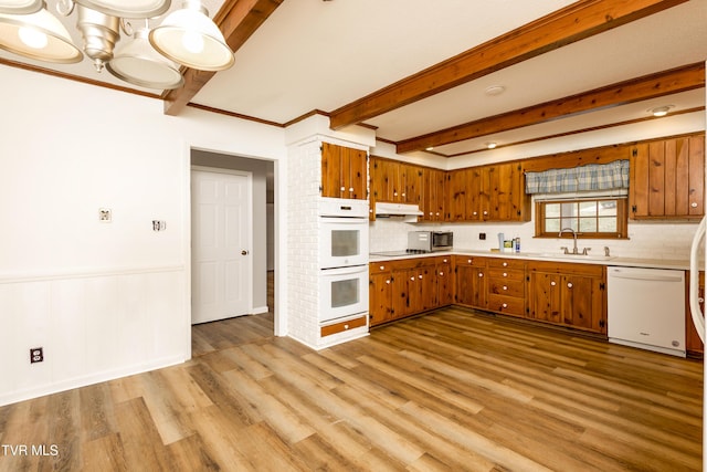 kitchen with a sink, white appliances, under cabinet range hood, and brown cabinetry