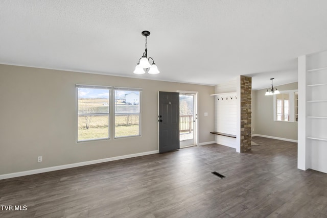 unfurnished living room featuring a wealth of natural light, a notable chandelier, dark wood finished floors, and visible vents