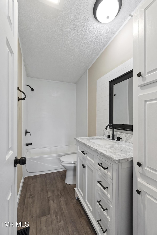 full bath with tub / shower combination, toilet, vanity, wood finished floors, and a textured ceiling